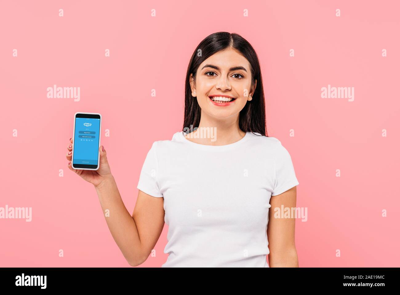 Kiev, UKRAINE - 20 septembre 2019 : jolie brunette smiling girl holding smartphone avec l'application Skype sur rose isolé Banque D'Images