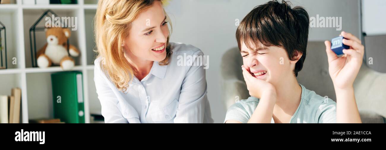 Vue panoramique tourné de kid de dyslexie holding building block et souriant en le regardant, psychologue pour enfants Banque D'Images