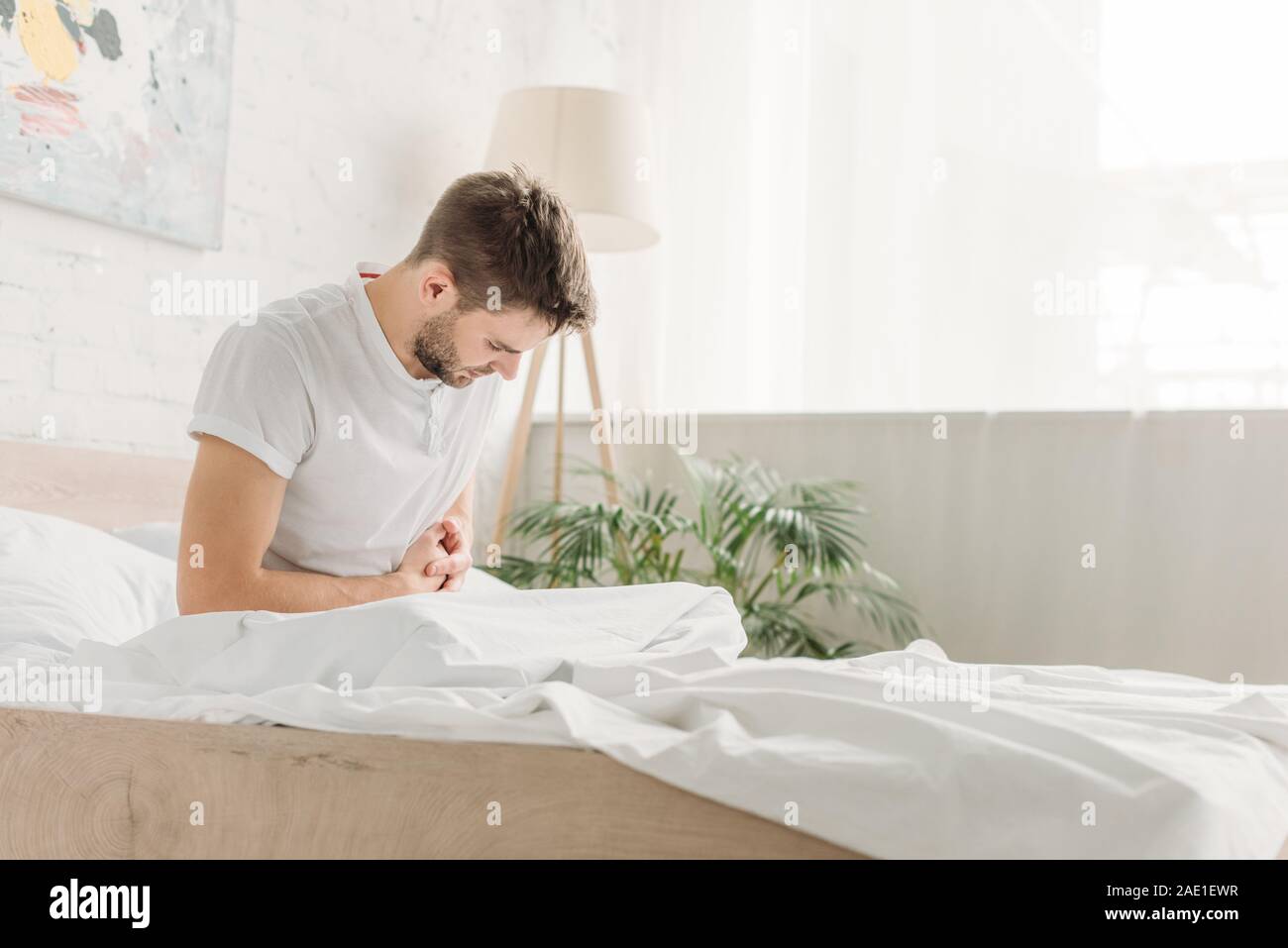 Jeune homme assis au lit et souffrant de douleurs abdominales Banque D'Images