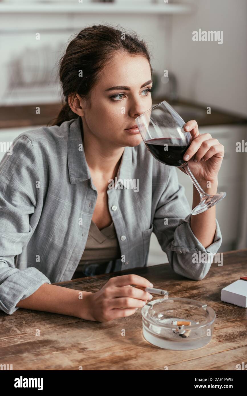 Pensive woman boire du vin et à fumer à table de cuisine Banque D'Images