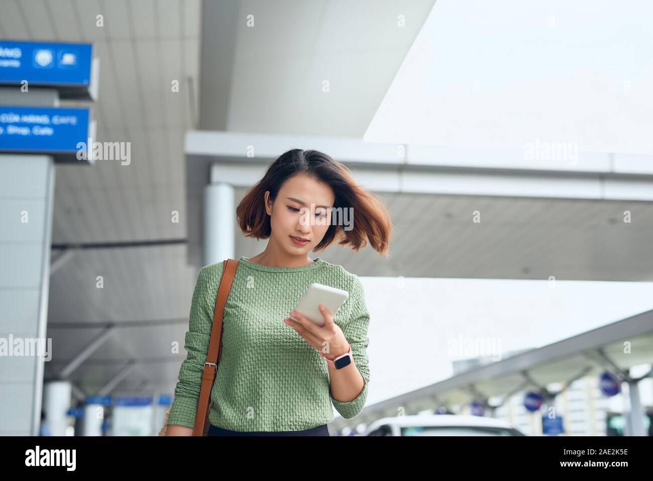 Asian Woman est la vérification sur son smartphone qu'elle attend dans airport de l'Asie. Banque D'Images