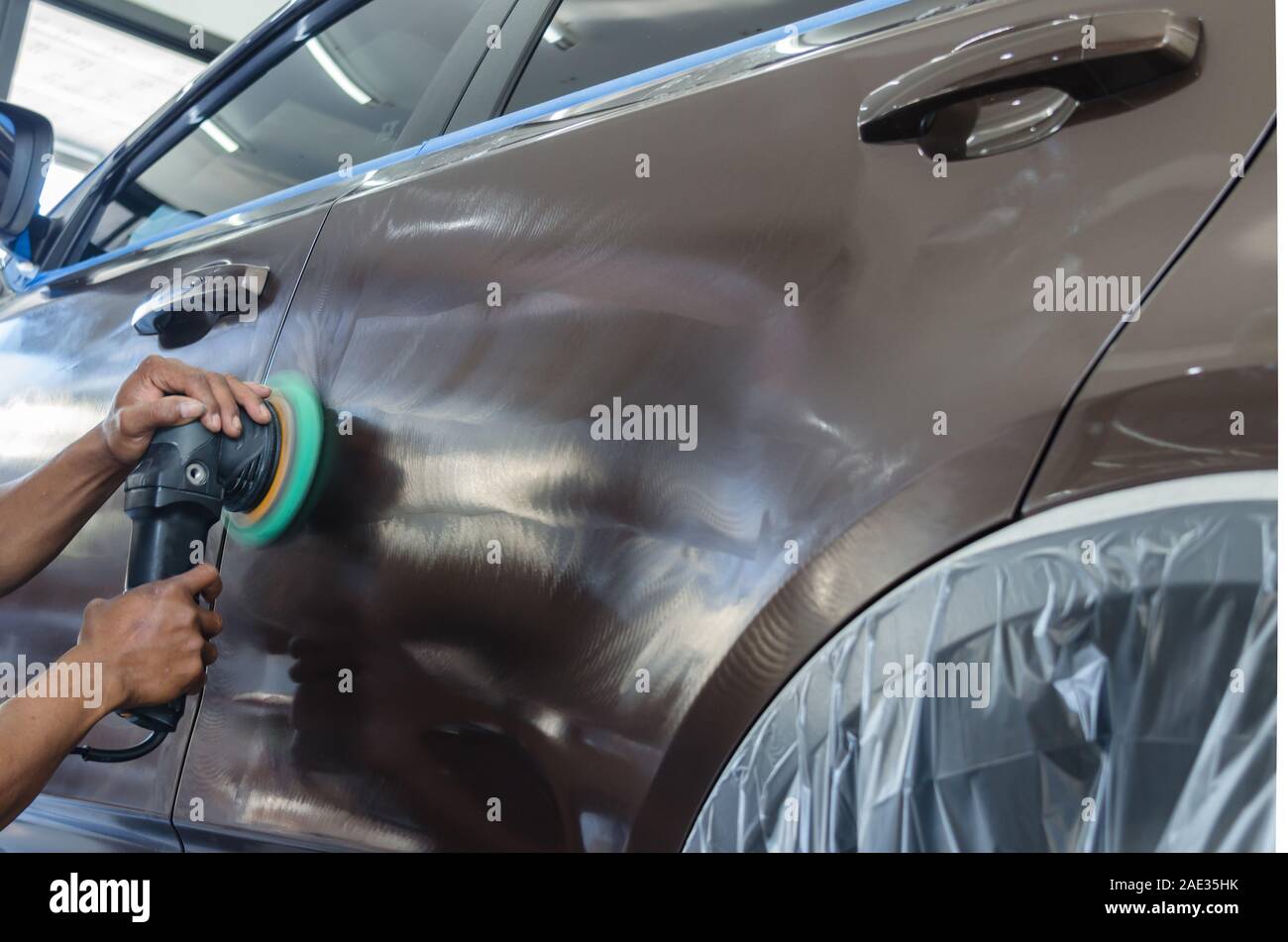 La suppression des rayures brun un homme tenant un outil de polissage automobile dans le garage Banque D'Images