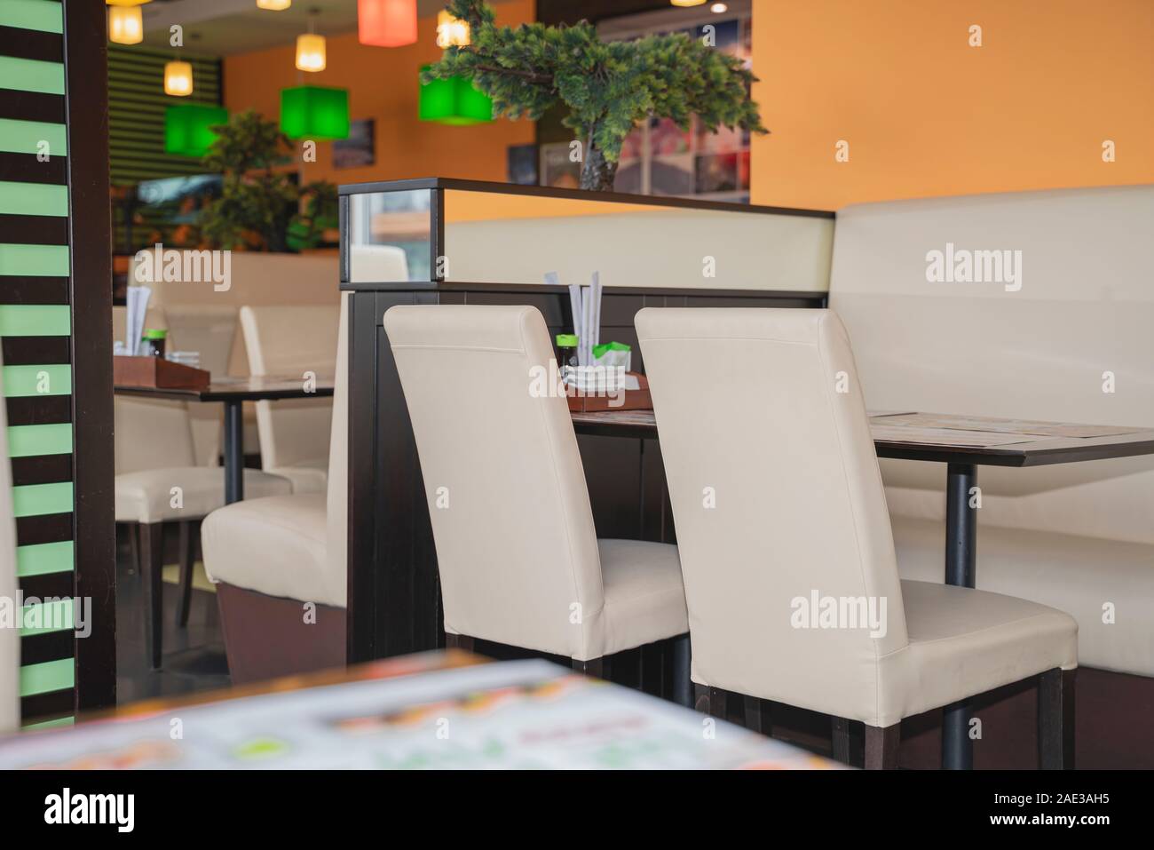 Fragment intérieur Café, vue sur table et chaises blanches sur fond de mur orange. Café est décoré avec des lampes multicolores et greenary Banque D'Images