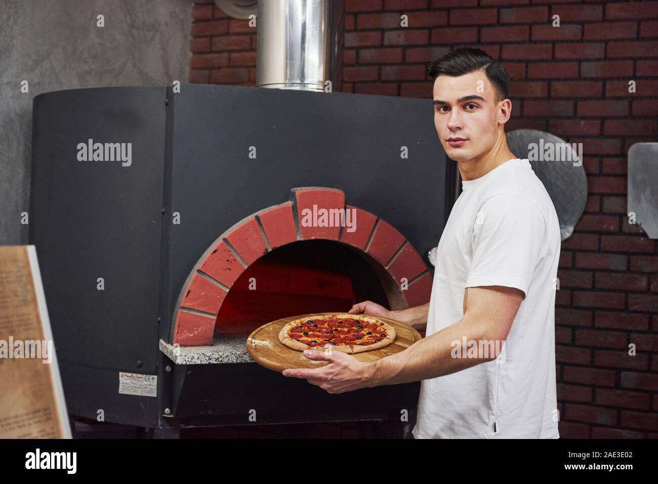 Baker en blanc élégant porter sort du four à pizza Banque D'Images