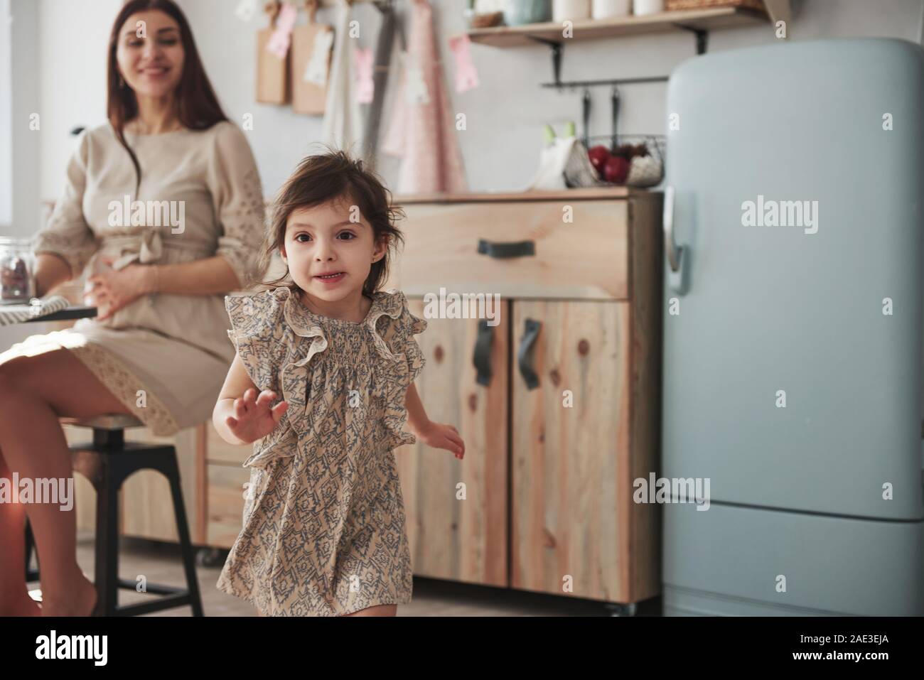 Enfant de sexe féminin ludique s'amuser en exécutant dans la cuisine le jour de devant sa mère Banque D'Images