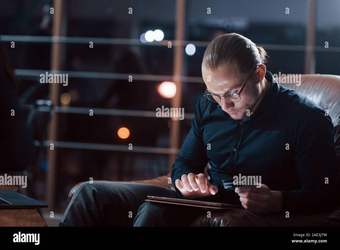 L'homme aux cheveux longs. Classy businessman dans eyewear travaille seul dans le bureau de la nuit, Banque D'Images