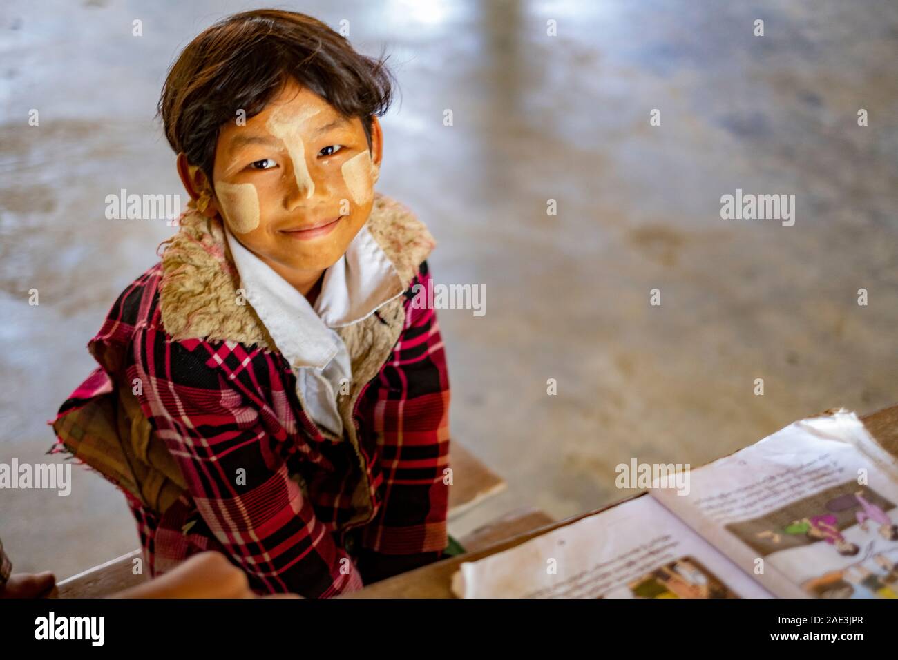 Smiling Young boy étudiant dans une école de village birman rurales le long de la rivière Chindwin, Myanmar (Birmanie) avec de la poudre de visage pour le protéger du soleil Banque D'Images