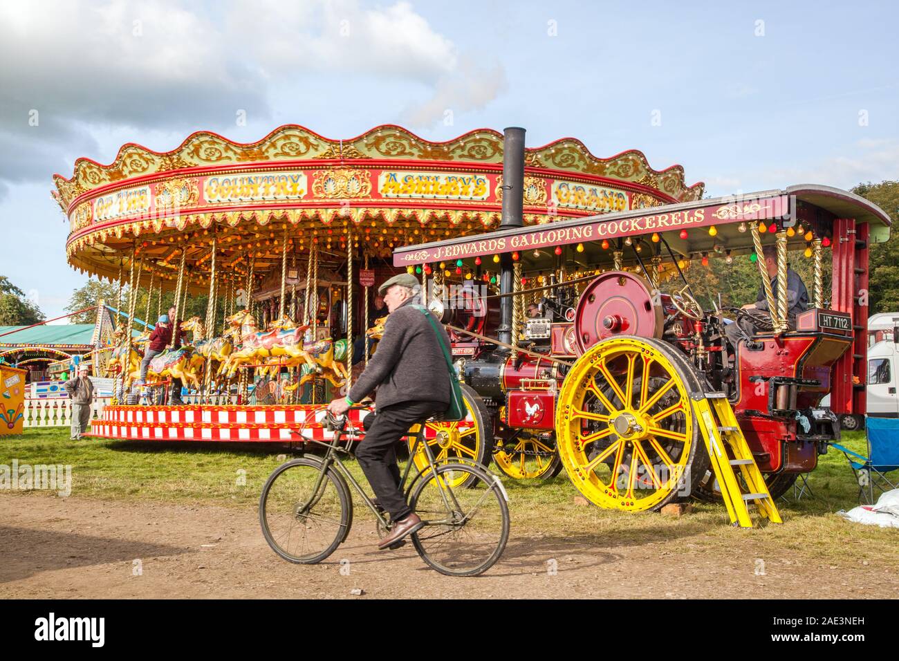 Old man riding bike randonnée à vélo dans un parc à vapeur vintage avec moteur de traction et rond-point carousal England UK Malpas Banque D'Images