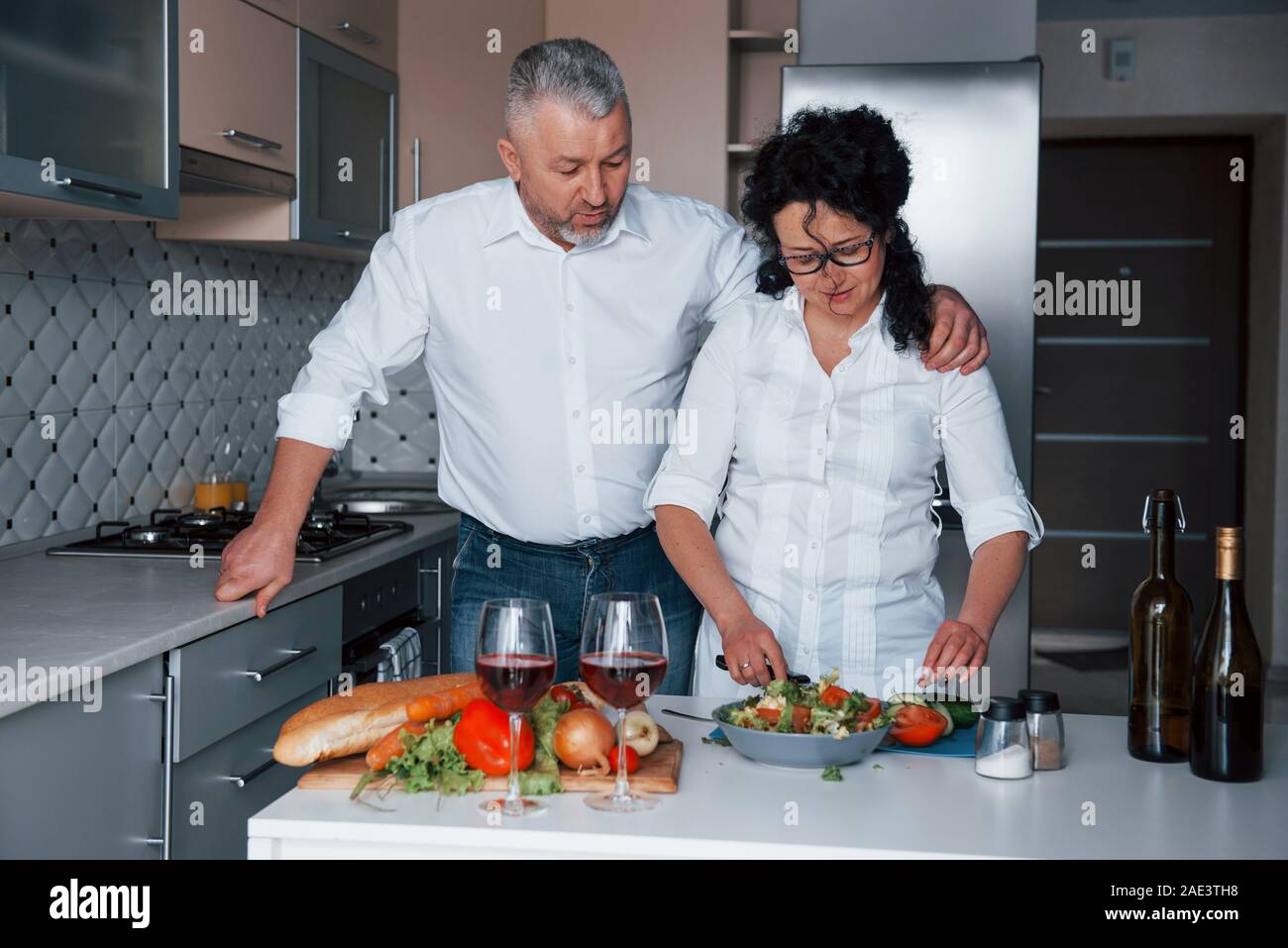 Faire une salade. L'homme et sa femme en chemise blanche à la préparation de la nourriture sur la cuisine en utilisant des légumes Banque D'Images