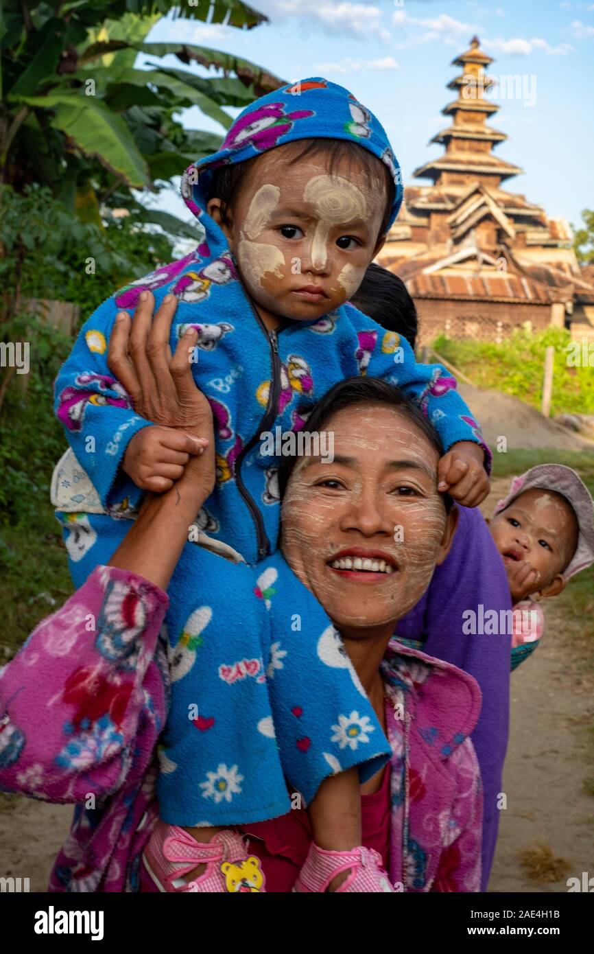 Une mère porte ses deux jeunes enfants à suivre un chemin rural avec leur visage avec un écran solaire, en poudre et avec un temple dans l'arrière-plan Banque D'Images