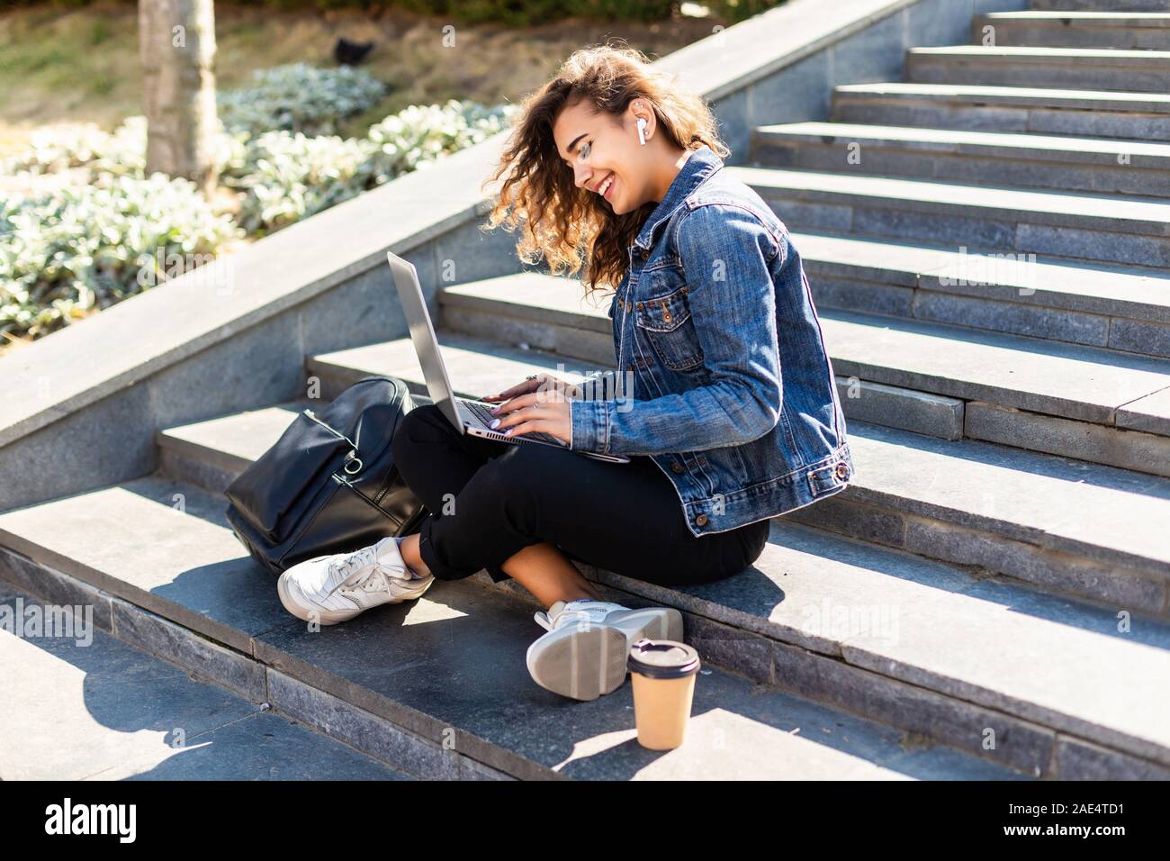 Jeune femme assise sur l'escalier avec un ordinateur portable sur la rue ensoleillée Banque D'Images