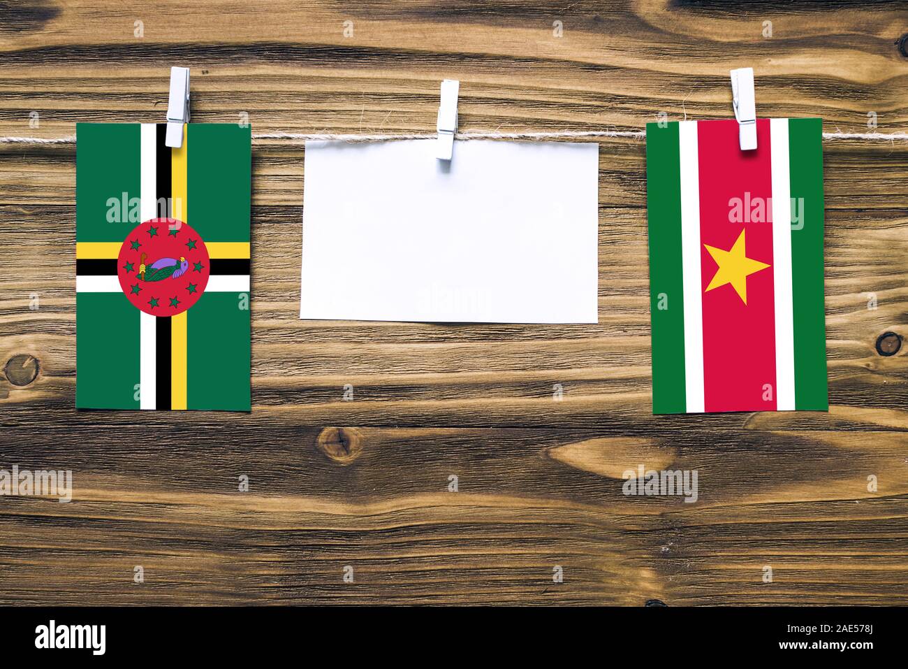 Drapeaux suspendus de la Dominique et le Suriname attaché à corde avec pinces à linge avec de l'espace de copie sur papier blanc sur fond de bois.rapport diplomatique Banque D'Images