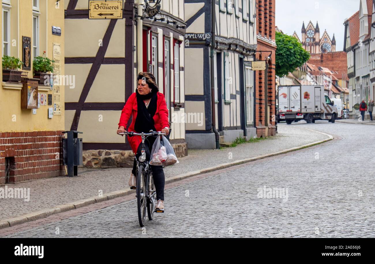 Vélo cycliste féminin transportant un sac commercial dans la ville historique de Tangermünde Saxe-Anhalt Allemagne Saxe-Anhalt Allemagne. Banque D'Images