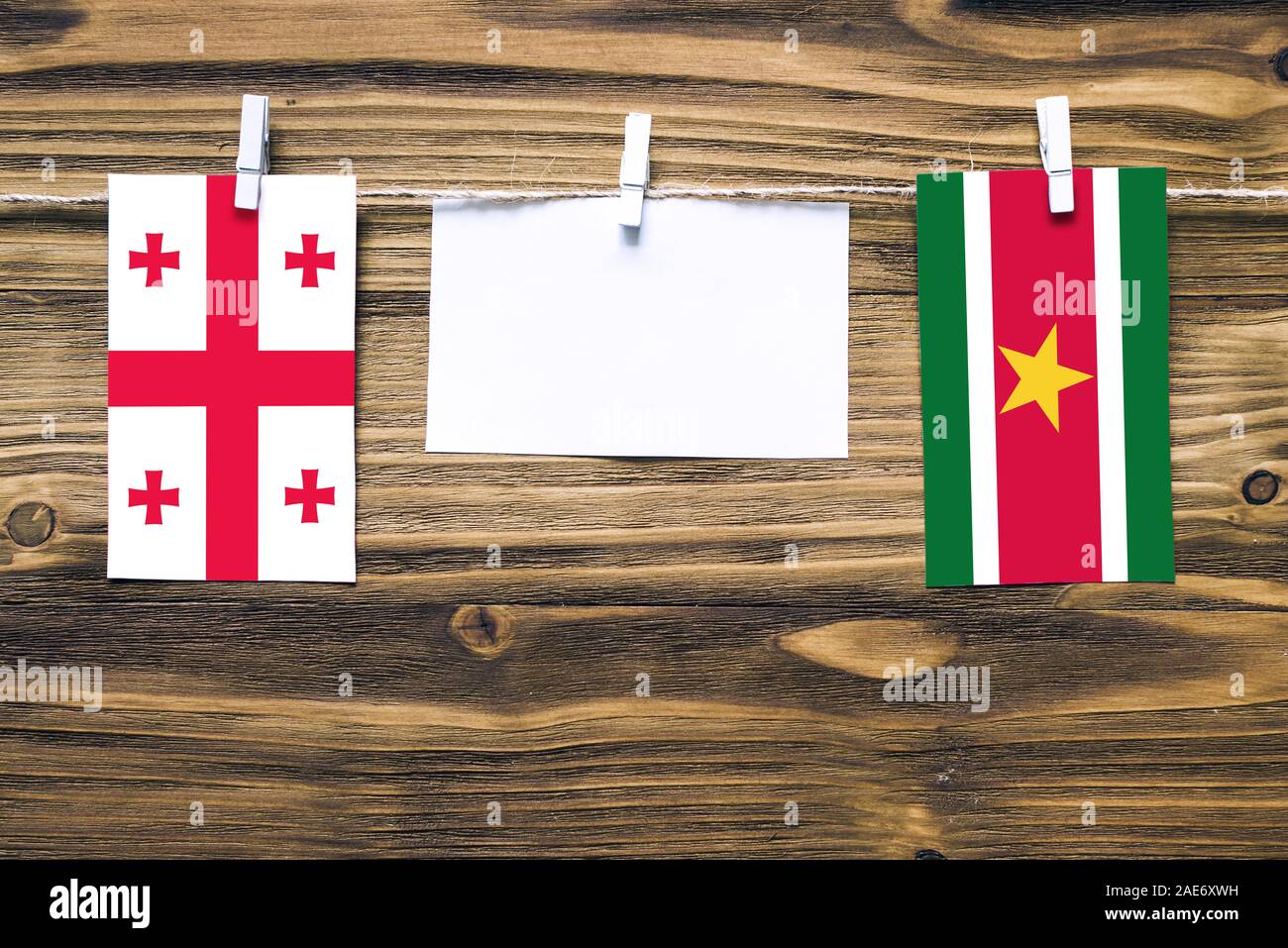 Drapeaux suspendus de la Géorgie et le Suriname attaché à la corde avec des pinces à linge avec de l'espace de copie sur papier blanc sur fond de bois.Les relations diplomatiques Banque D'Images