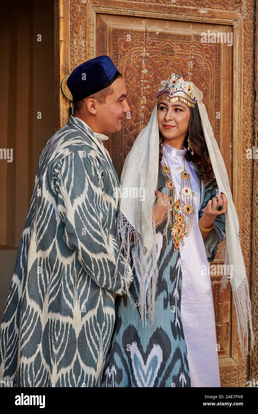Couples nuptiales en vêtements traditionnels posant devant de la célèbre place du Registan, Samarkand, Ouzbékistan, l'Asie centrale Banque D'Images