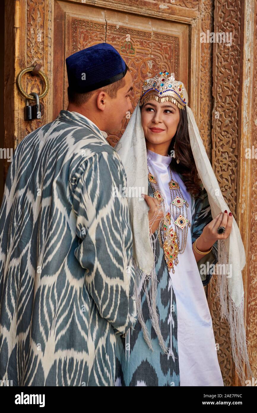 Couples nuptiales en vêtements traditionnels posant devant de la célèbre place du Registan, Samarkand, Ouzbékistan, l'Asie centrale Banque D'Images