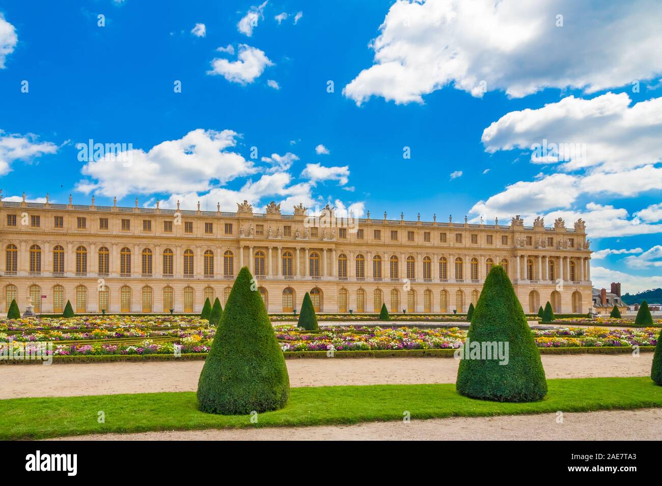 Vue panoramique parfaite de la façade de l'aile sud du château de Versailles avec un sentier de gravier, pelouse, fleurs et arbres en forme de cône, typique de... Banque D'Images