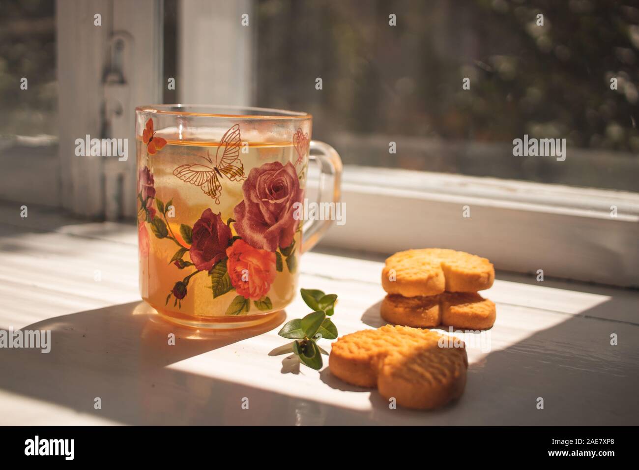Thé aux herbes. Une tasse en verre avec plateau se tient sur le rebord. Des biscuits en forme de coeur Banque D'Images