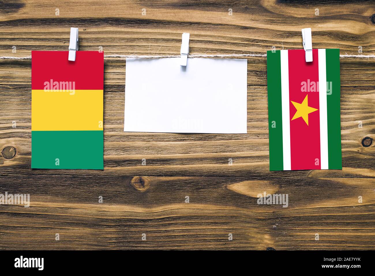 Drapeaux suspendus de Guinée et le Suriname attaché à la corde avec des pinces à linge avec de l'espace de copie sur papier blanc sur fond de bois.Les relations diplomatiques Banque D'Images