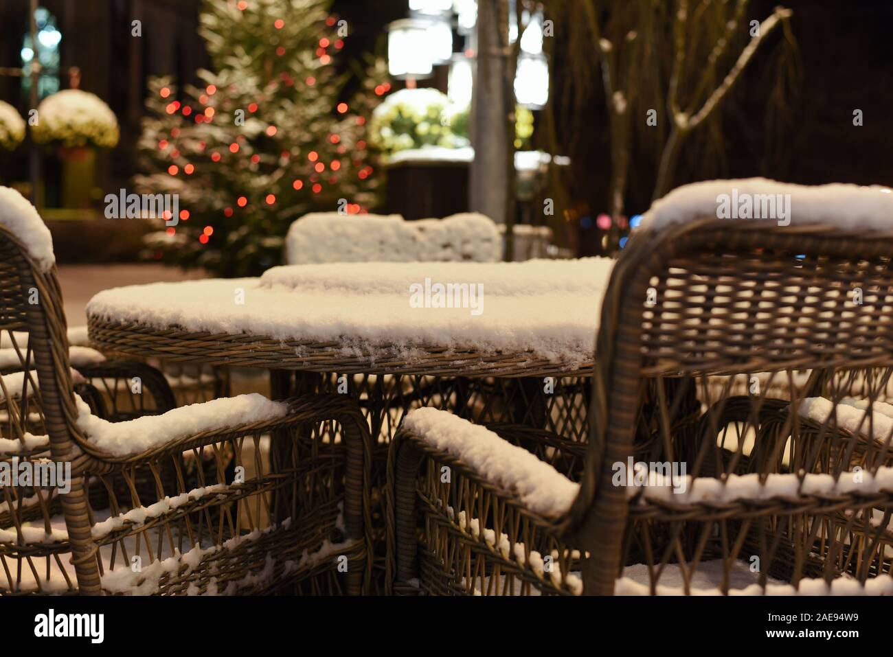 Chaises en osier et un café de la rue table sur une nuit d'hiver glaciale neige sur la Noël et le Nouvel An eve, festif de la lumière sur l'arrière-plan Banque D'Images