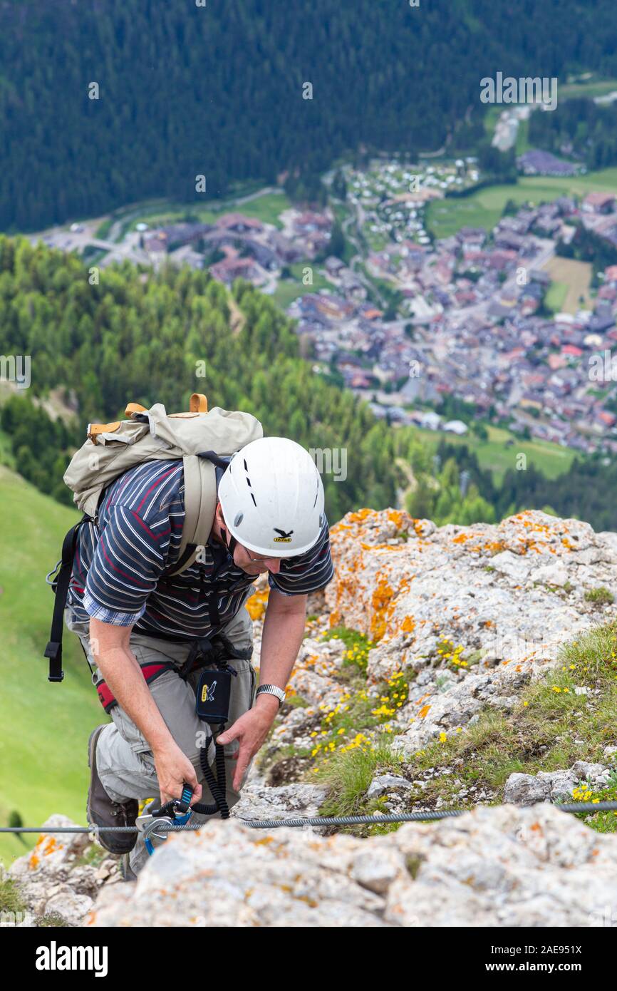 CANAZEI, ITALIE - Juillet 5,2013 : un grimpeur avec un casque et un sac à dos accroché sur une corde fixe en acier et en arrière-plan le village au bas de t Banque D'Images