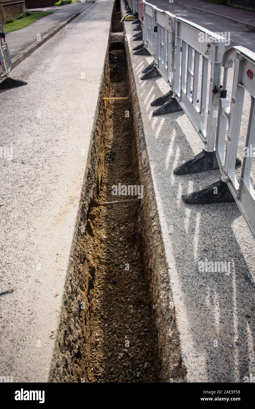 Longue tranchée profonde à travers la surface de la route, encordée par des barrières en plastique, en attendant l'installation d'une nouvelle conduite de gaz. Banque D'Images