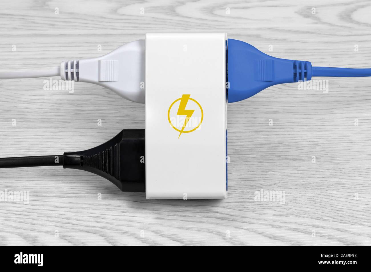 Un câble bleu, un noir et un blanc connecté à une prise multiple sur un fond de bois blanc, avec un symbole de l'énergie jaune sur la prise Banque D'Images