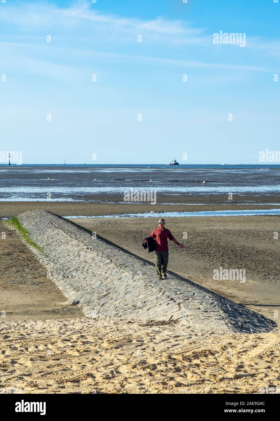 Homme debout sur un goyne en pierre à marée basse à la plage Océan Atlantique Cuxhaven Basse-Saxe Allemagne. Banque D'Images