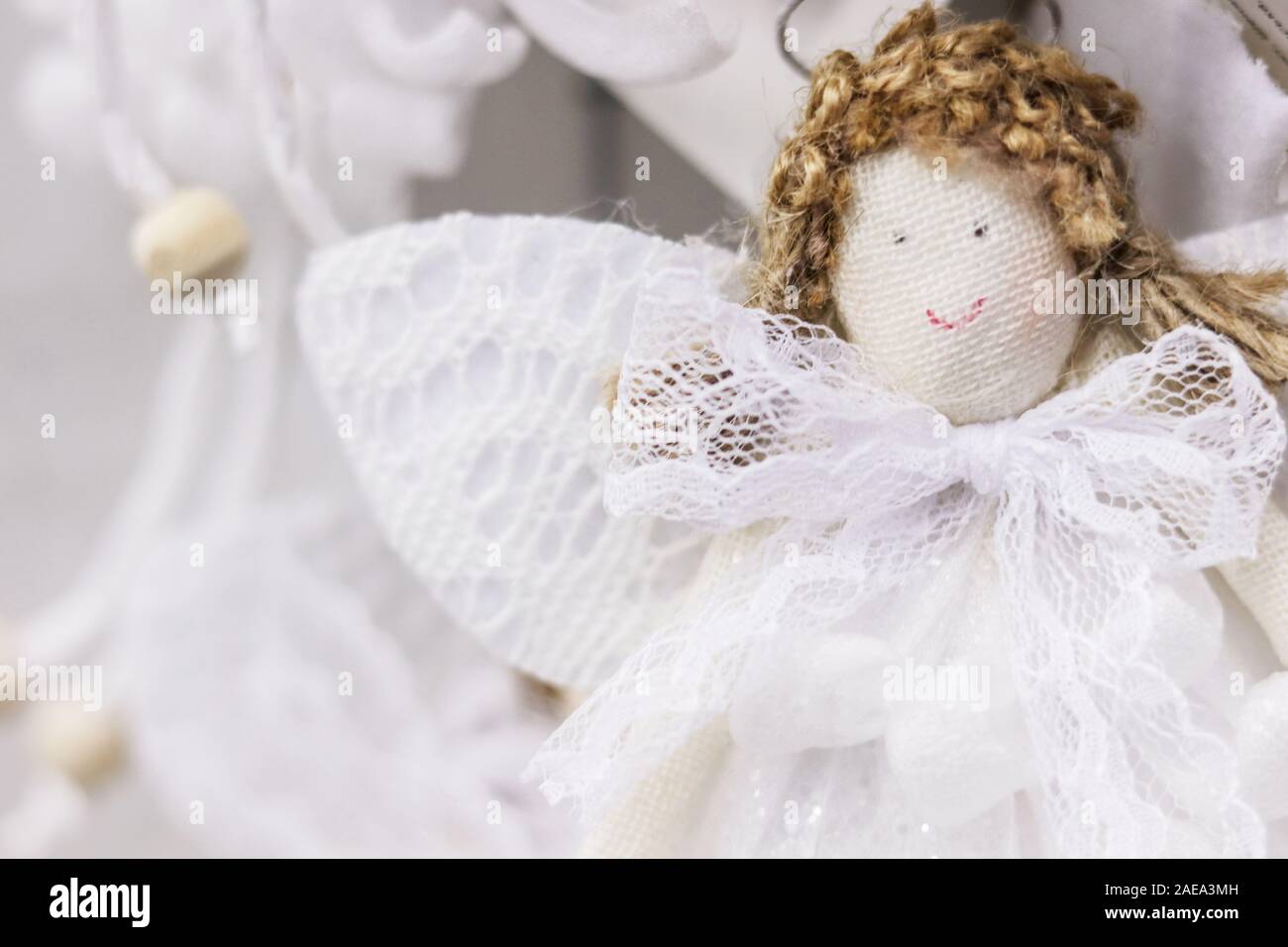 Jolie poupée en tissu ange fait main avec cheveux bouclés, ailes en dentelle blanche et robe. Fond décoratif de Noël à mise au point douce Banque D'Images