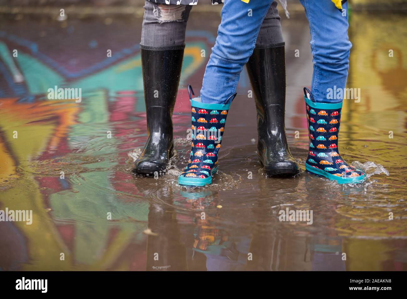 Garçon enfant et femme dans Drôle de bottes en caoutchouc debout dans la  flaque dans la rue après la pluie. Dans la famille des bottes de caoutchouc  colorés dans une grande flaque