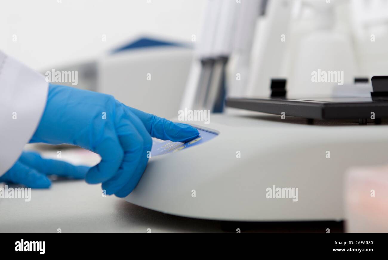 Les mains dans des gants en latex à presser des boutons sur la machine de laboratoire Banque D'Images