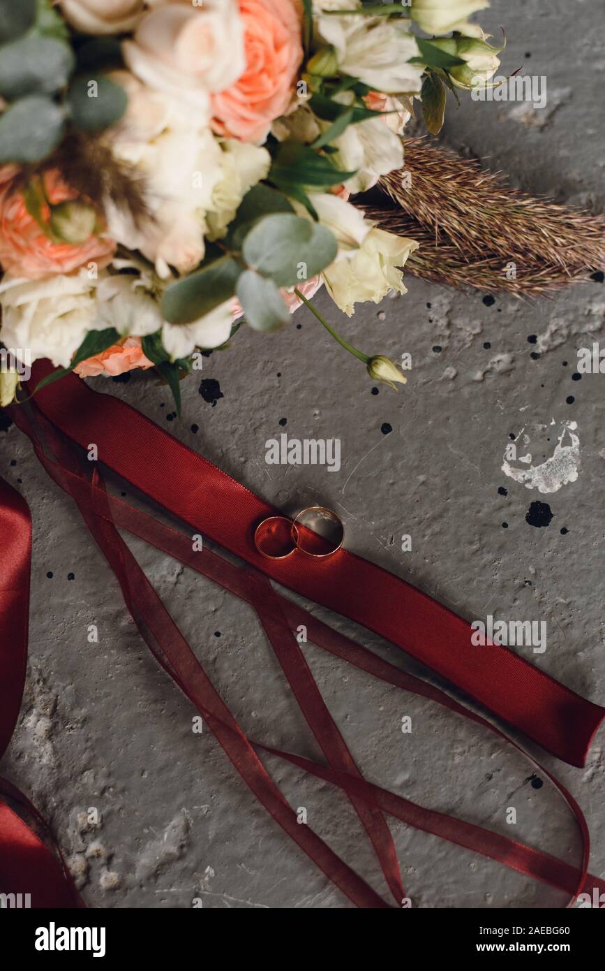 Des anneaux les mariés sur un arrière-plan gris grunge fond et d'un bouquet de brides. Banque D'Images