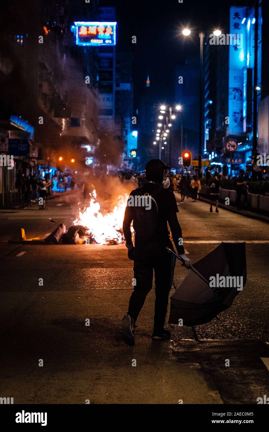 Hong Kong - le 17 novembre 2019 : Un manifestant masqué avec parapluie debout à feu, utilisé comme barricade au cours de la protestation de HongKong 2019 Banque D'Images