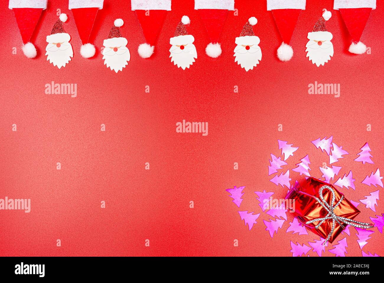 Chapeaux de Père Noël et le père Noël fait face à du matériel disposés en une rangée sur le dessus et un cadeau enveloppé dans le coin inférieur droit étendu sur purple Christma Banque D'Images