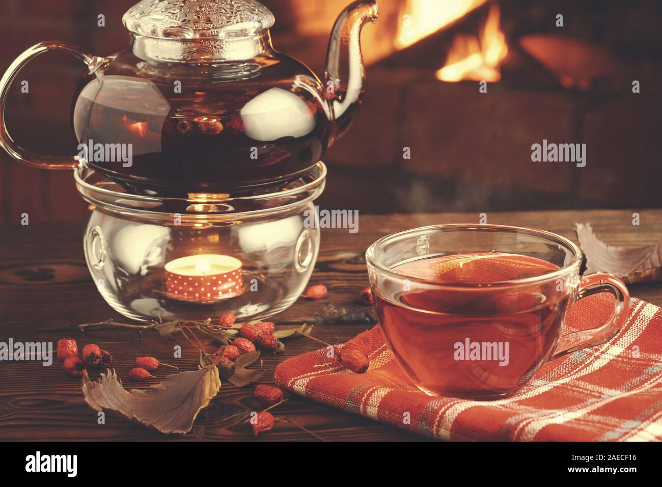 Plateau avec l'aubépine dans un verre tasse et théière avec un photophore sur une table en bois dans une chambre avec une cheminée. Banque D'Images