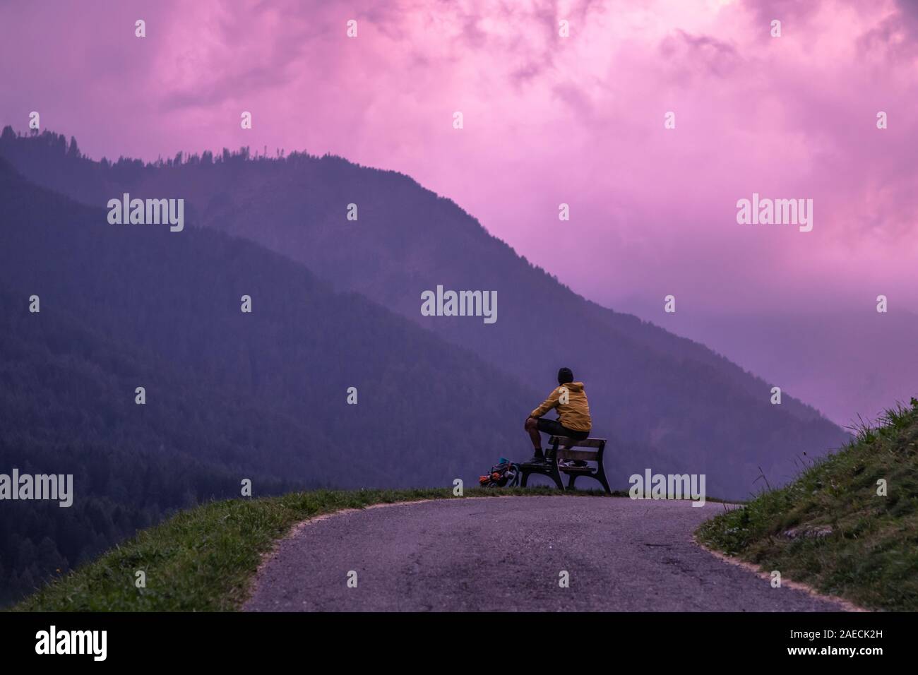 Jeune homme assis sur un banc en face de la montagne après le coucher du soleil avec purple sky. ,Dolomites Tyrol du Sud, Italie Banque D'Images