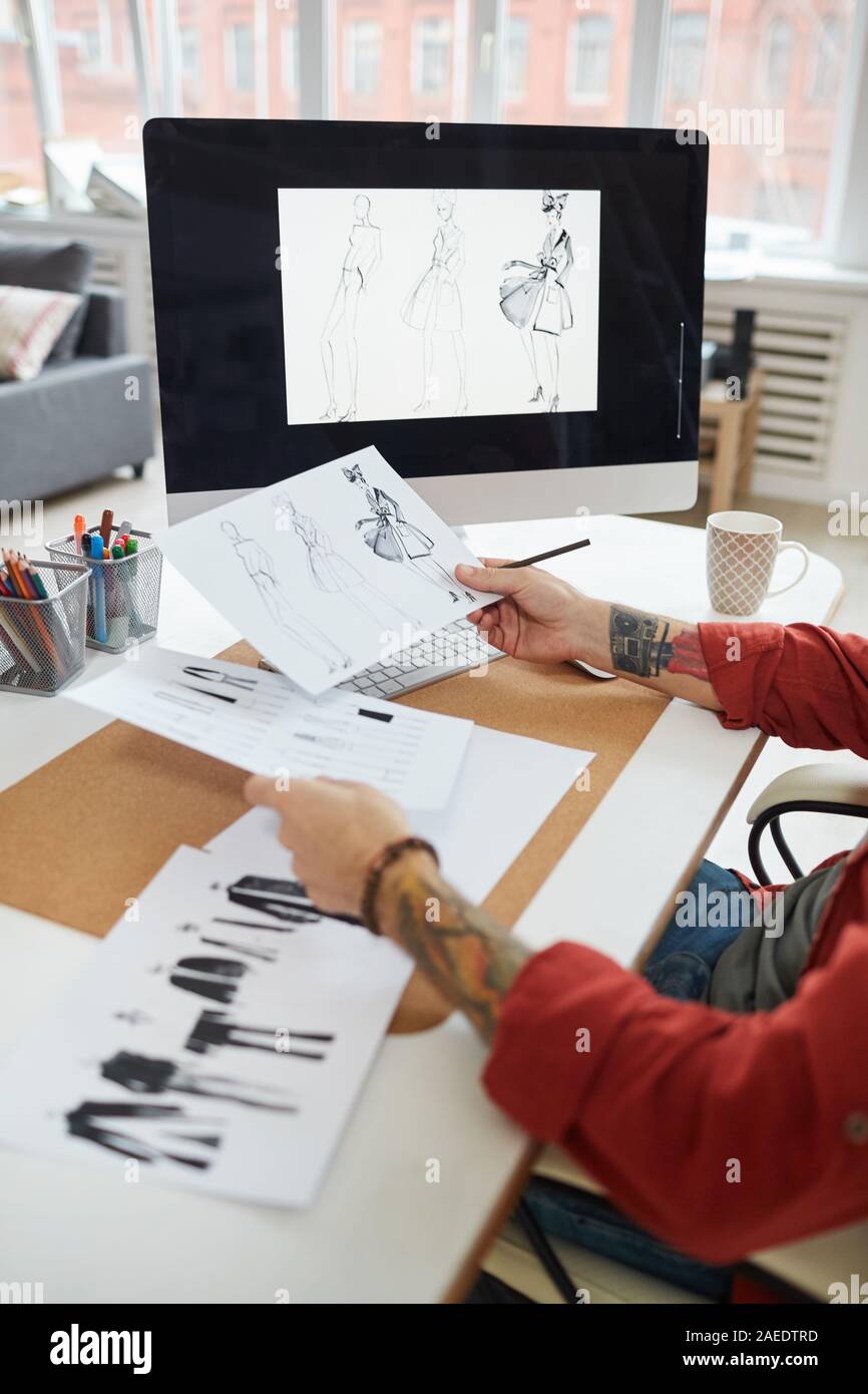Gros plan Vue de côté de l'homme tatoué mains tenant lieu de travail en plus de croquis de mode atelier ou design studio, copy space Banque D'Images