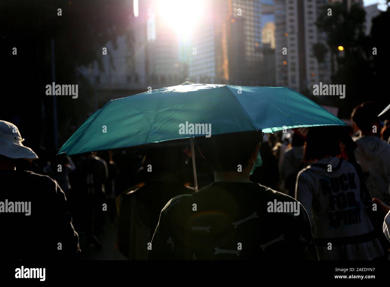 On peut voir un manifestant tenant un parapluie bleu, éclairé par la lumière du soleil. Ce rassemblement a marqué l'anniversaire de six mois de protestations à Hong Kong. Banque D'Images