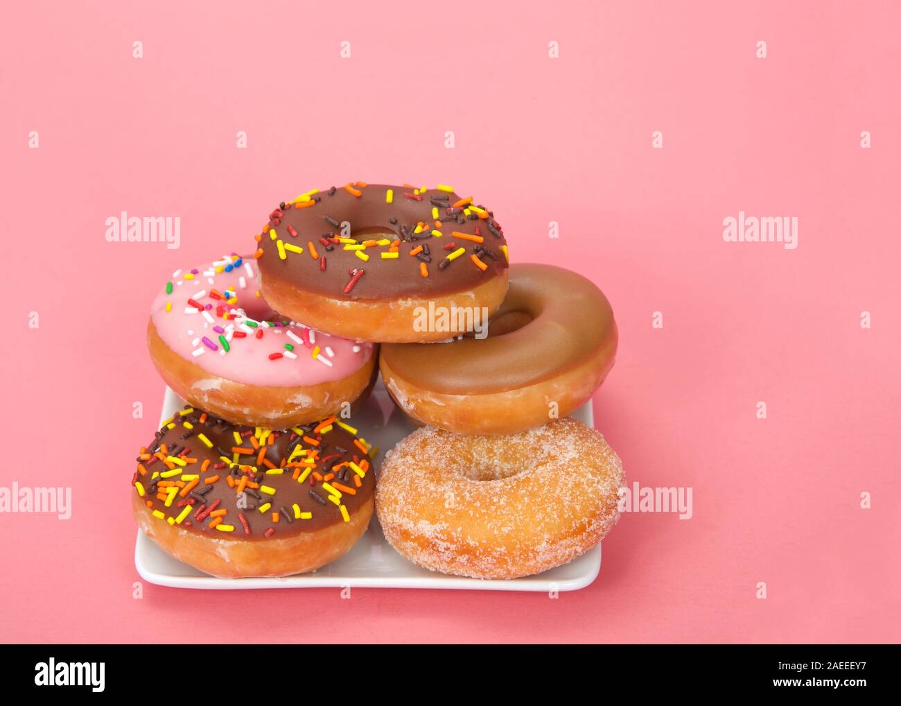 Petite plaque carrée avec donuts empilés, différentes saveurs. Fond rose avec copie espace. Banque D'Images