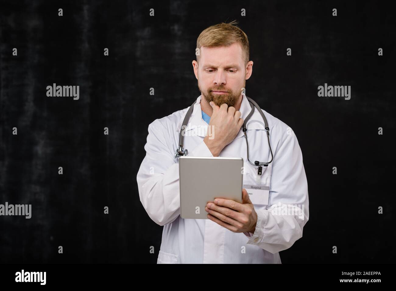 Pensive young doctor avec phonendoscope sur le cou à la recherche de données en ligne Banque D'Images