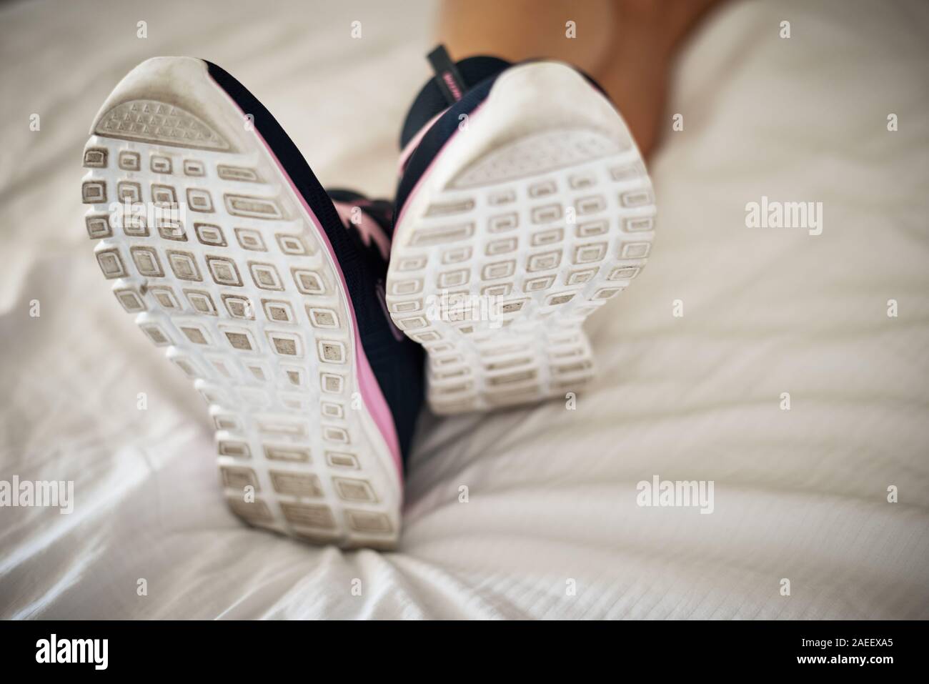 Femme en chaussures de sport sale couché sur un couvre-lit blanc dans une chambre d'hôtel Banque D'Images