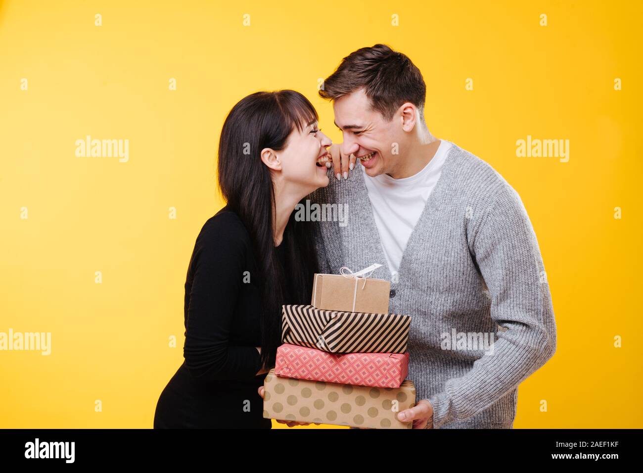Happy young couple laughing, tout en échangeant des cadeaux sur fond jaune Banque D'Images