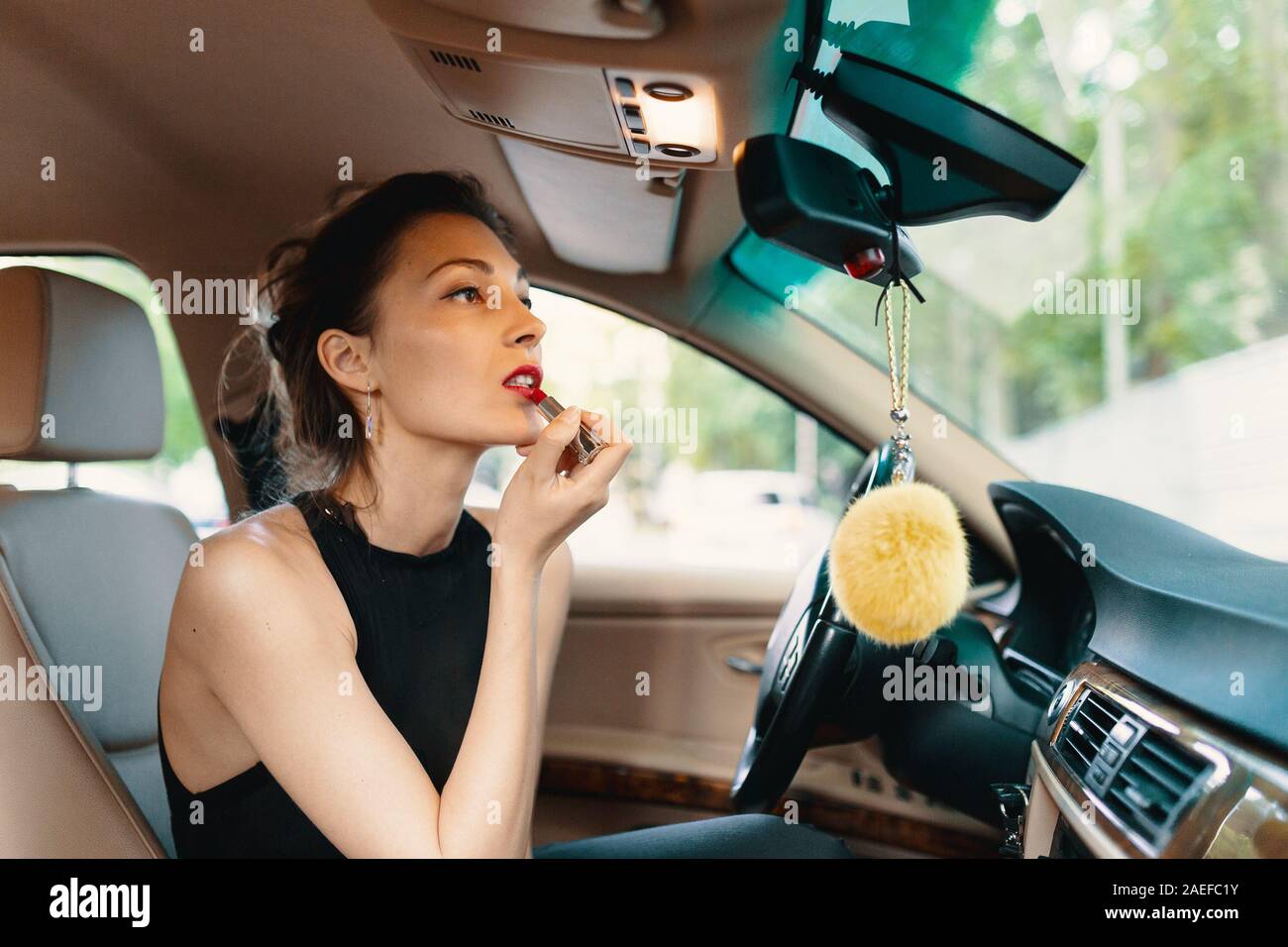 Jeune femme élégante à rétroviseur en peinture ses lèvres faisant l'application constituent en conduisant la voiture. Banque D'Images
