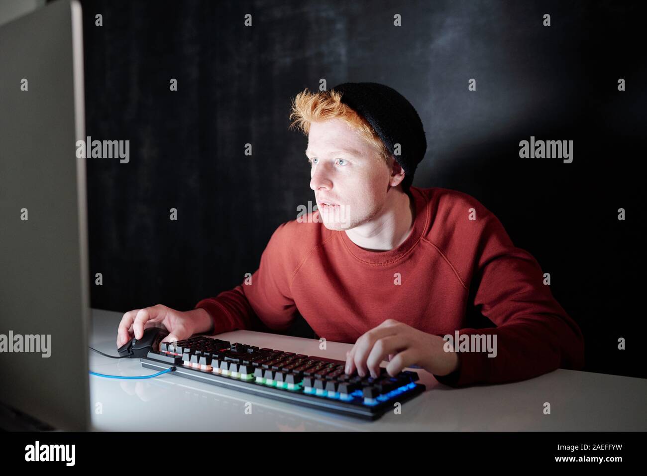 Guy en noir et black beanie appuyer sur les touches de clavier et de cliquer sur une souris Banque D'Images