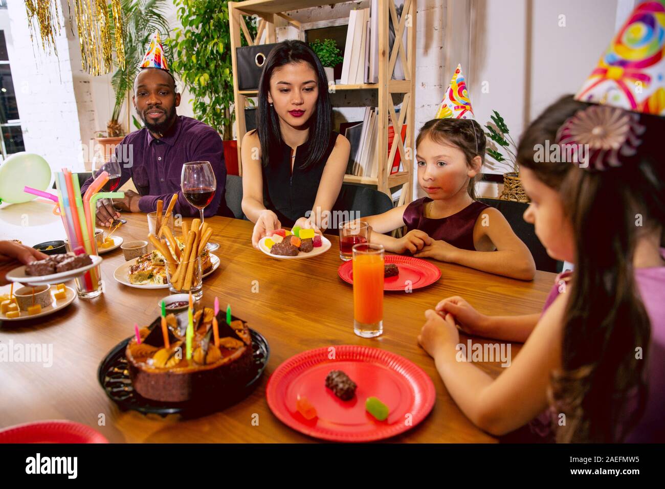 Portrait of happy famille multiethnique fêter un anniversaire à la maison. Grande famille de manger des collations et de boire du vin tout en s'amusant et d'accueil des enfants. Célébration, famille, parti, home concept. Banque D'Images