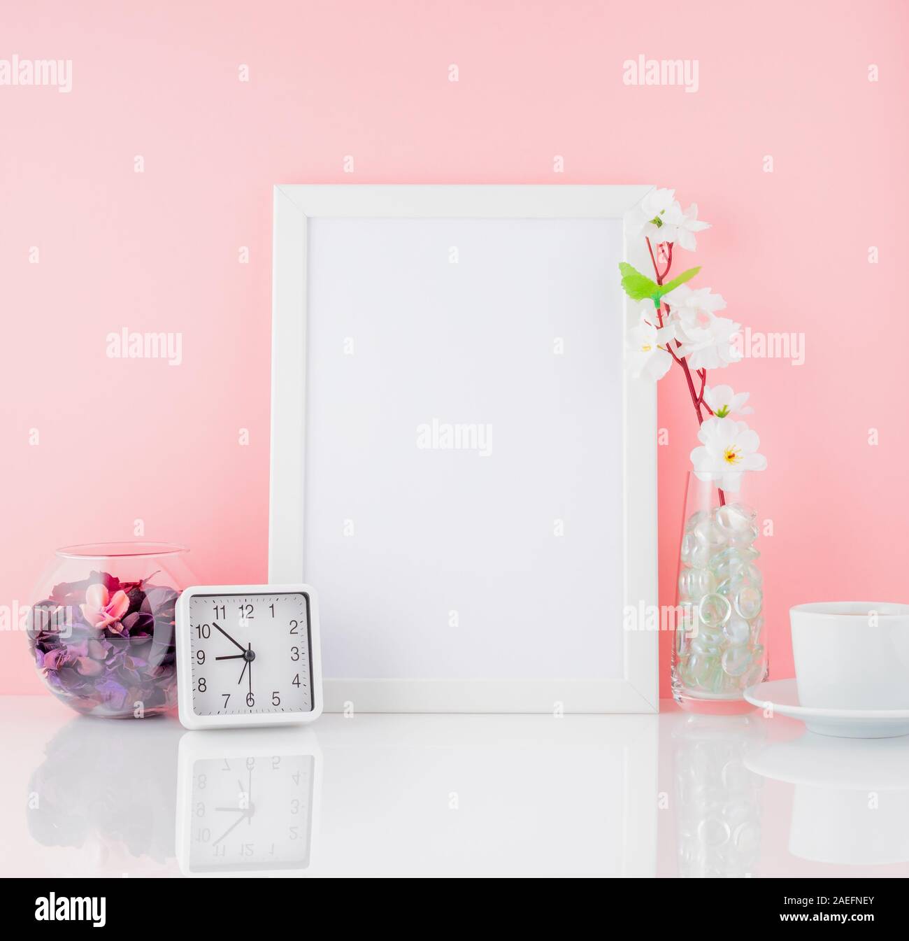 Cadre blanc vierge, fleur, réveil et tasse de café ou de thé sur un tableau blanc contre le mur rose avec copie espace. Des maquettes. Banque D'Images