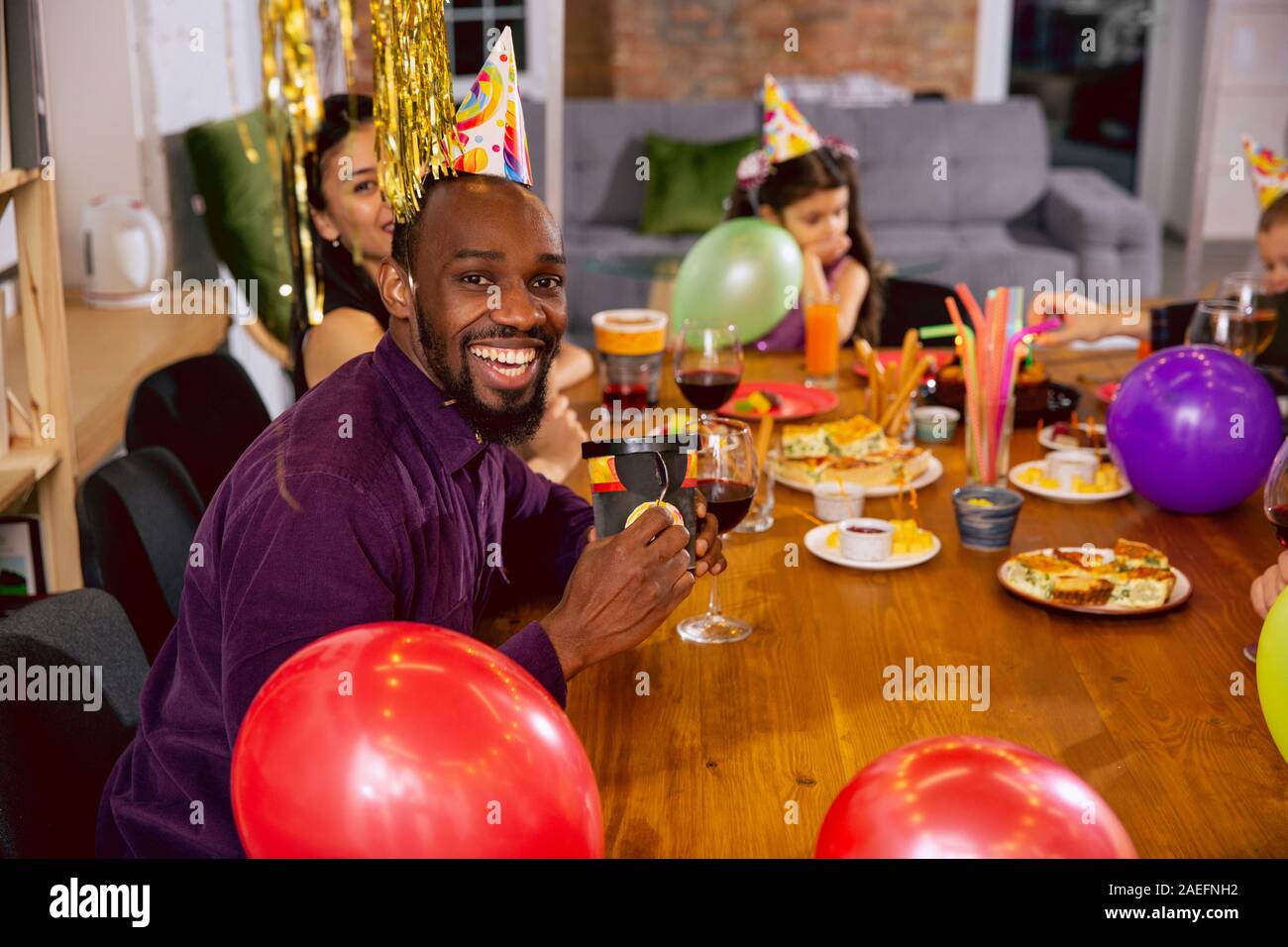 Portrait of happy famille multiethnique fêter un anniversaire à la maison. Grande famille de manger des collations et de boire du vin tout en s'amusant et d'accueil des enfants. Célébration, famille, parti, home concept. Banque D'Images