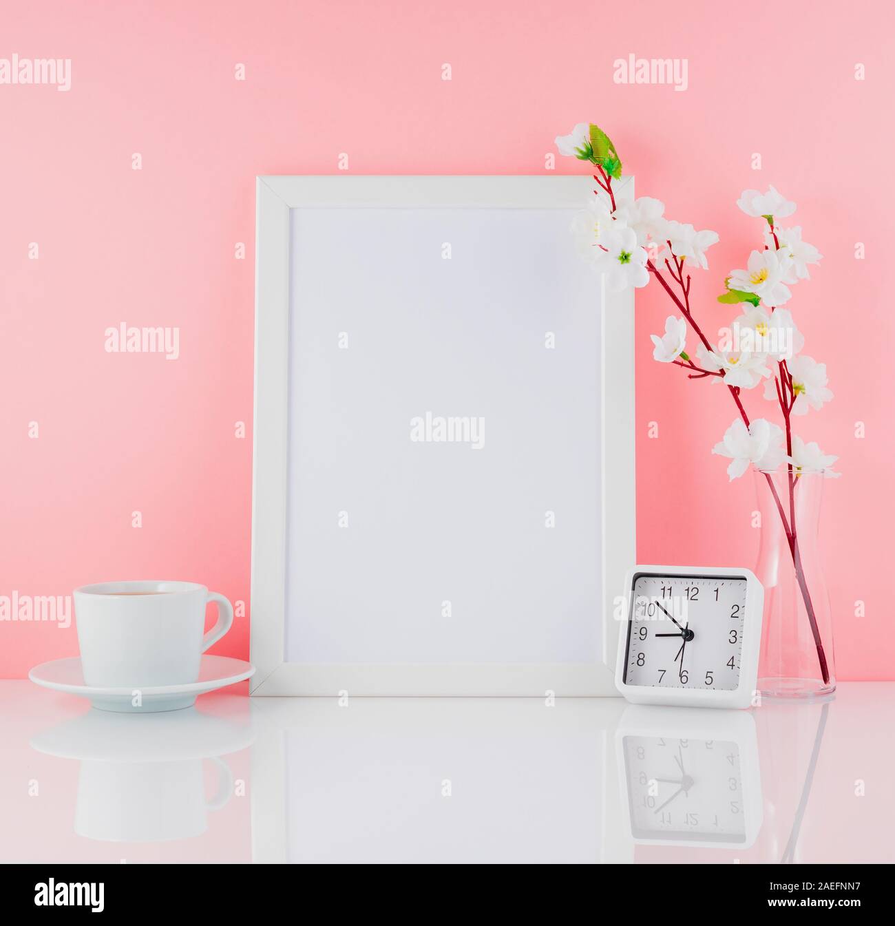 Cadre blanc vierge, fleur, réveil et tasse de café ou de thé sur un tableau blanc contre le mur rose avec copie espace. Des maquettes. Banque D'Images