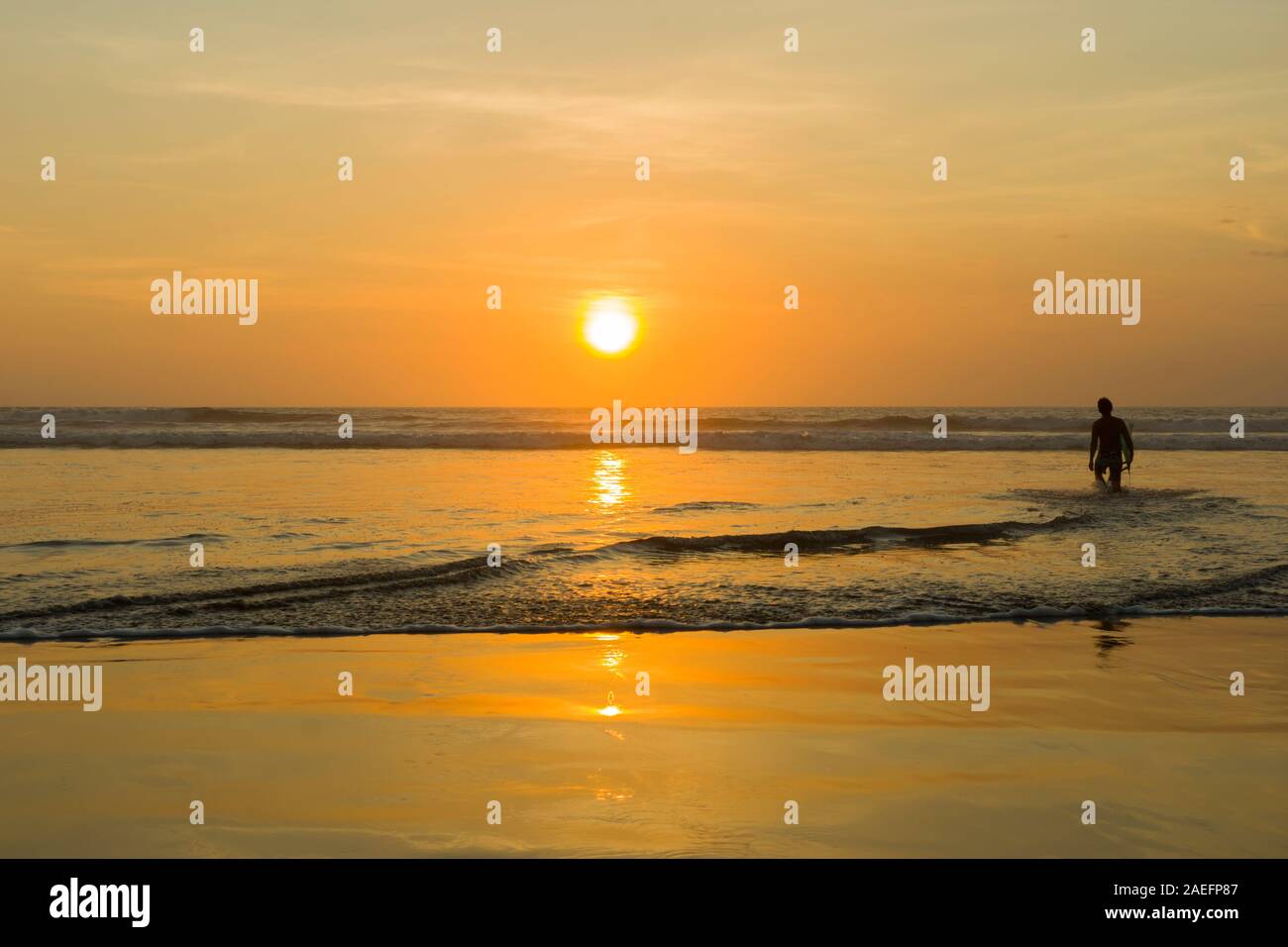 Silhouette d'un surfer carrying his surfboard sur Kuta Beach à un coucher du soleil d'or Banque D'Images