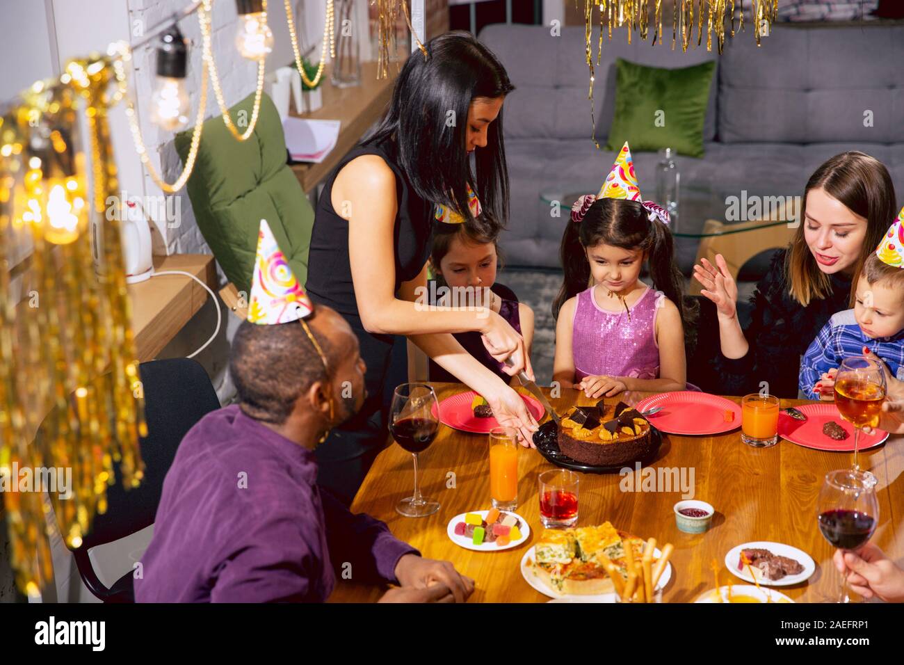 Portrait of happy famille multiethnique fêter un anniversaire à la maison. Grande famille de manger des gâteaux et boire du vin tout en s'amusant et d'accueil des enfants. Célébration, famille, parti, home concept. Banque D'Images